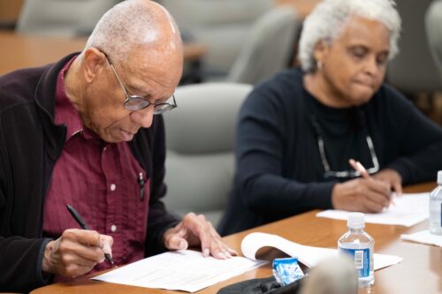 An African American man and woman writing at a table at the listening session in Pittsburgh, PA for ICC